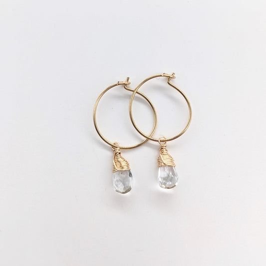 A woman wearing the Mini-hoop Aqua Quartz Charm Earrings in 14k Gold Filled, stacked with an ear cuff and huggie earring.