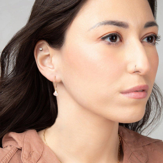 A woman wearing the Mini-hoop Rose Quartz Charm Earrings in 14k gold filled. The earrings are visible on her right ear.