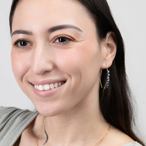 A smiling woman wearing the Mai Blue Beaded Threader Earrings in 14k Gold Filled. A smiling woman wearing the Mai Blue Beaded Threader Earrings in 14k Gold Filled.