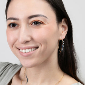 A smiling woman wearing the Mai Blue Beaded Threader Earrings in 14k Gold Filled. A smiling woman wearing the Mai Blue Beaded Threader Earrings in 14k Gold Filled.