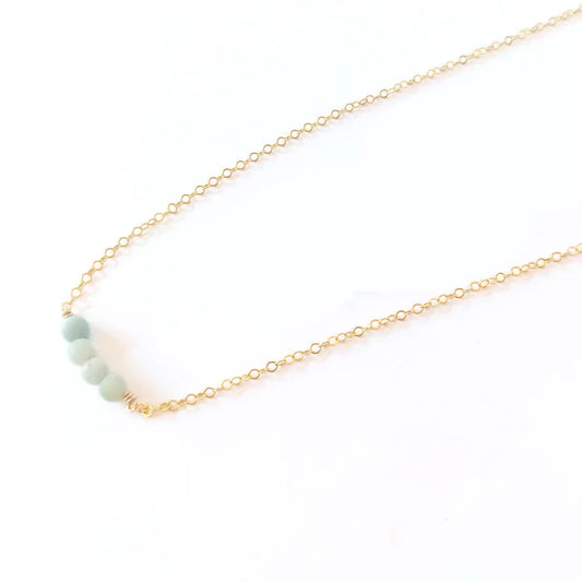 Close-up of woman in beige zippered top wearing a minimalist14k gold filled necklace with four amazonite gemstones.