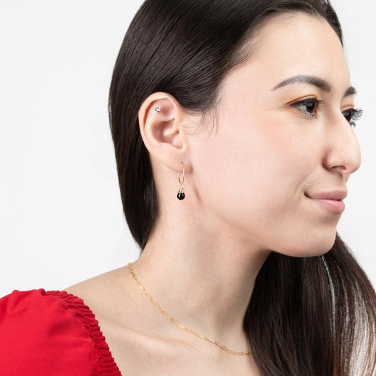 A woman in red wearing the Mini-hoop Midnight Black Charm Earrings with 14k gold filled hoops.