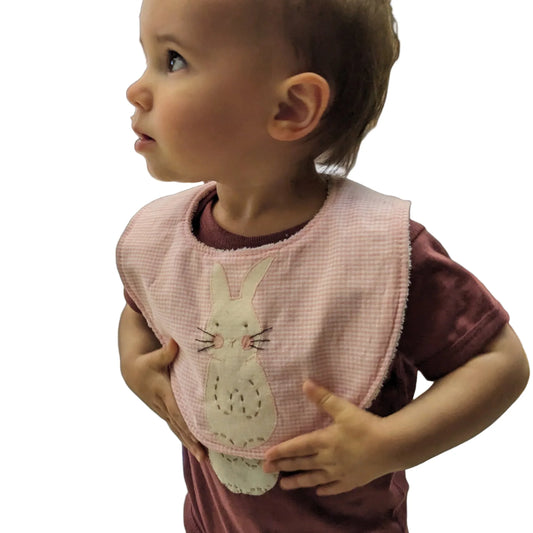 A pink baby bib with a handstitched bunny applique on the front, made of pink gingham fabric with a terry cloth back.