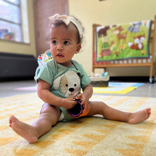 Baby wearing sage green cotton onesie with handmade puppy applique sitting on a yellow rug.