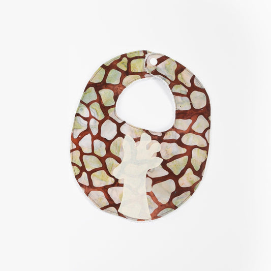 A baby sitting on the floor wearing a giraffe print bib with off-white giraffe applique and a plush terry cloth back.