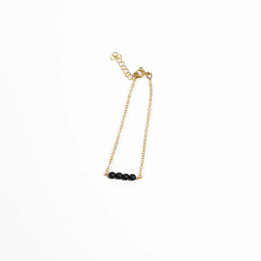 Woman in a black and white striped shirt showcasing a 14k gold filled minimalist bracelet with four black onyx beads.