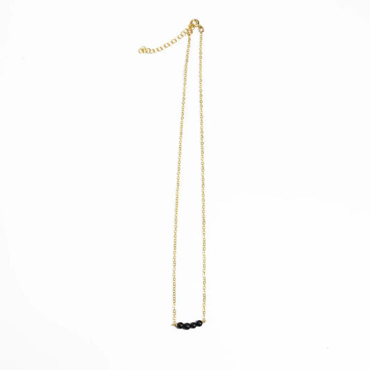 Woman in a black and white striped shirt wearing Jordan Black Onyx Necklace, Bracelet, and J Hoop Earrings in 14k gold filled.