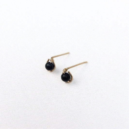 close up of a model wearing stud earrings made of a black onyx bead encircled in 14 karat gold filled wire