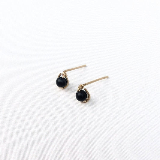 close up of a model wearing stud earrings made of a black onyx bead encircled in 14 karat gold filled wire