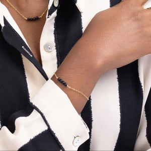 Woman in a black and white striped shirt showcasing a 14k gold filled minimalist bracelet with four black onyx beads. Woman in a black and white striped shirt showcasing a 14k gold filled minimalist bracelet with four black onyx beads.