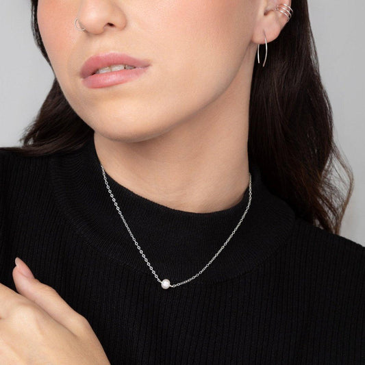 A woman in a black top wearing the Leeda Pearl Necklace in Sterling Silver which features a classic single freshwater pearl