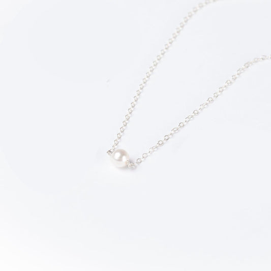 A woman in a black top wearing the Leeda Pearl Necklace in Sterling Silver which features a classic single freshwater pearl