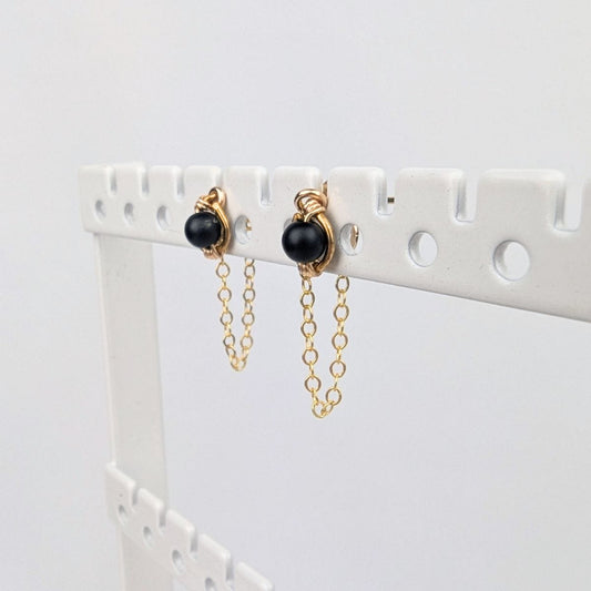 a pair of gold stud earrings on a display rack with dainty chain earring jackets attached to form loops.