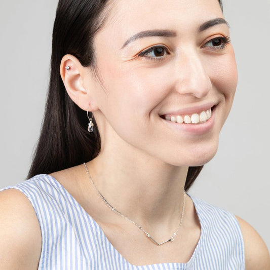 A woman in a blue and white striped top wearing the Mini-Hoop Aqua Quartz Charm Earrings in Sterling Silver, smiling and looking off to the side.