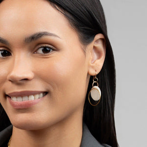 Woman wearing Hadeelah Porcelain Earrings, dangling hoops of brass encircling a disc of porcelain clay. Woman wearing Hadeelah Porcelain Earrings, dangling hoops of brass encircling a disc of porcelain clay.