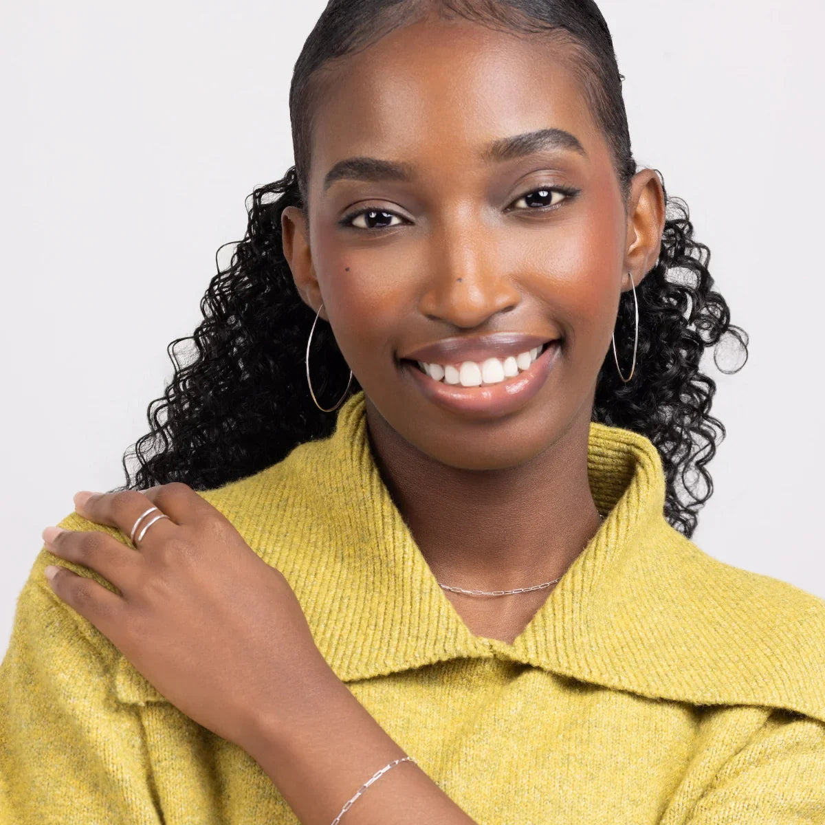 A woman in a chartreuse sweater wearing Azmera Hammered Hoop Earrings in Sterling Silver.