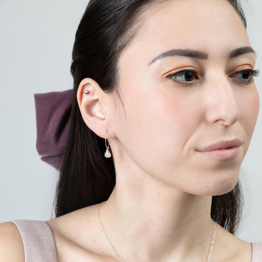 A woman wearing Mini-hoop Rose Quartz Charm Earrings, showcasing her right ear.