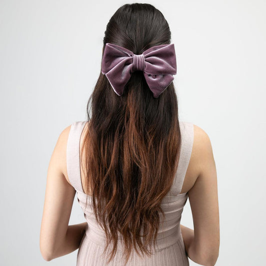 Woman with long hair is seen from the back, wearing a rose gold velvet hair bow barrette in their hair.