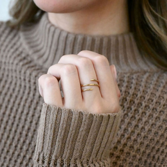 photo of model's hand wearing brown sweater and shiny brass wrap ring