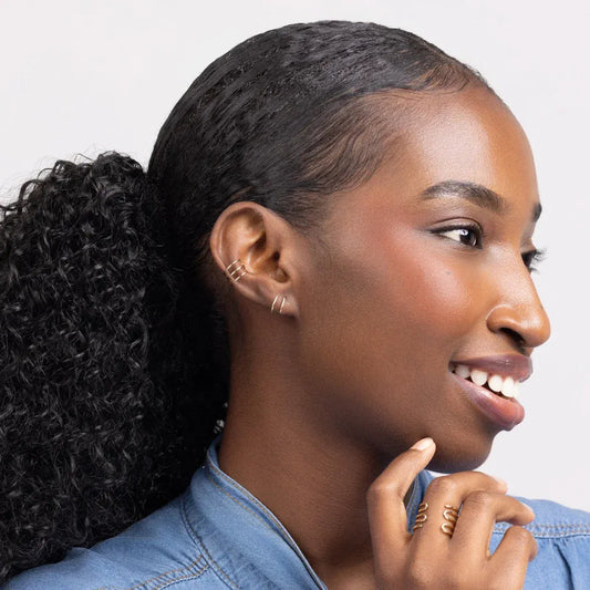 Woman in a blue denim shirt wearing Journey of Hope Huggie Earrings in 14k gold filled.