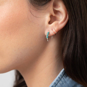 A close-up image of a woman's ear wearing a sterling silver huggie earring and threader earring with a small turquoise bead detail. A close-up image of a woman's ear wearing a sterling silver huggie earring and threader earring with a small turquoise bead detail.