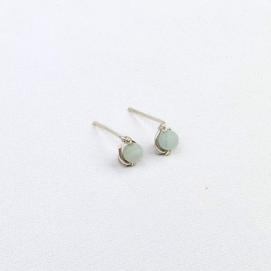 brunette model wearing silver stud earrings with a blue green bead, as well as two silver necklaces