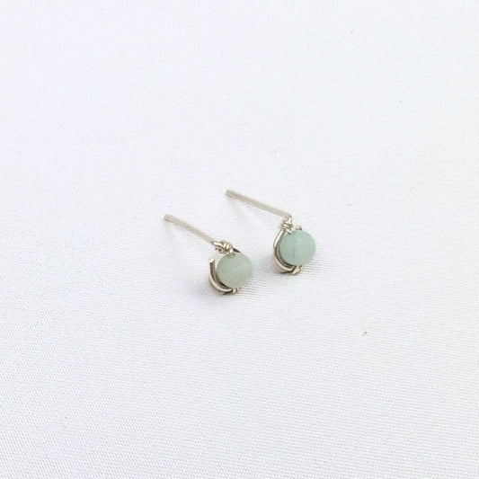 brunette model wearing silver stud earrings with a blue green bead, as well as two silver necklaces
