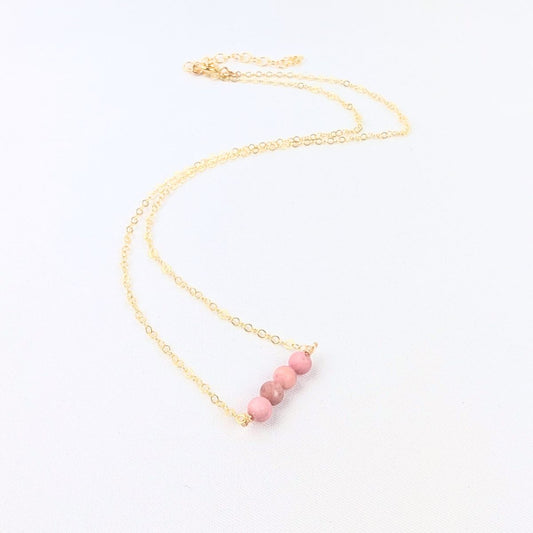 Necklace with pink beads on a gold chain against a white background