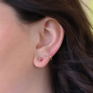 Close-up of an ear wearing a small pink earring and gold hoop. Close-up of an ear wearing a small pink earring and gold hoop.