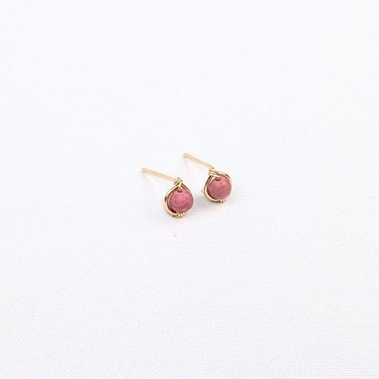 Close-up of an ear wearing a small pink earring and gold hoop.
