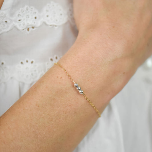 Gold bracelet with 3 silver beads on a white background