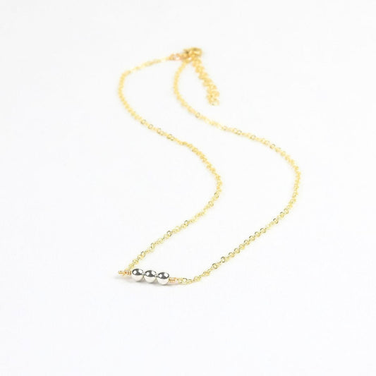 Gold necklace with three silver beads on a white background
