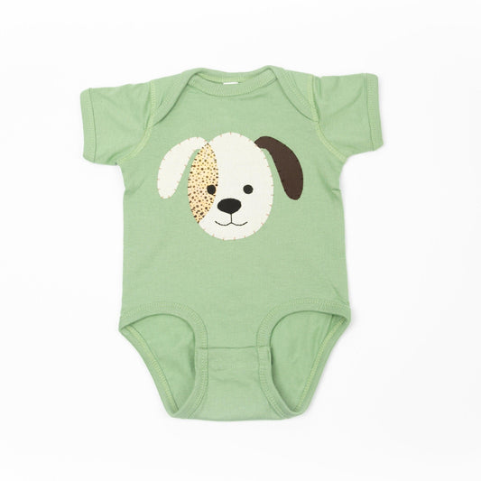 Baby wearing sage green cotton onesie with handmade puppy applique sitting on a yellow rug.
