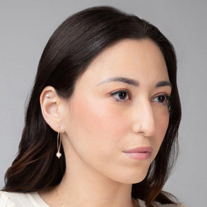 A young woman wearing Rana Pearl Threader Earrings in 14k gold filled, which are hanging from the ear and have a small freshwater pearl detail. A young woman wearing Rana Pearl Threader Earrings in 14k gold filled, which are hanging from the ear and have a small freshwater pearl detail.
