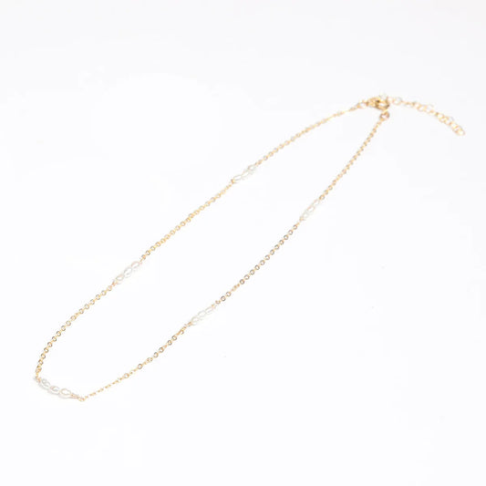 A woman in a white lace top showcasing a 14k gold filled necklace with freshwater rice pearl stations.