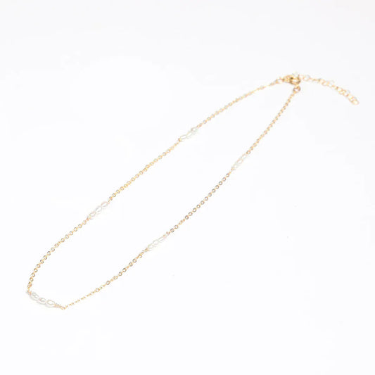 A woman in a white lace top showcasing a 14k gold filled necklace with freshwater rice pearl stations.