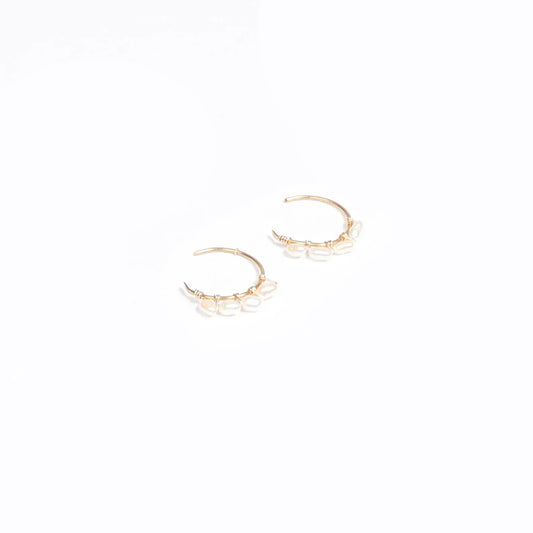 A woman wearing a pair of 14k gold filled C hoop earrings with rice pearls.