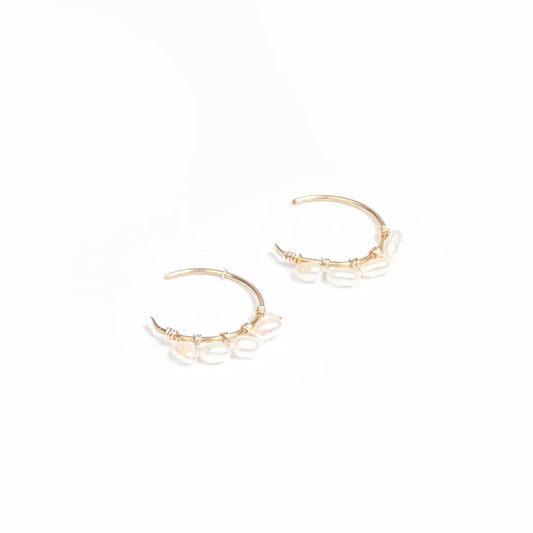 A woman wearing a pair of 14k gold filled C hoop earrings with rice pearls.