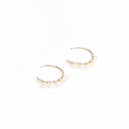 A woman wearing a pair of 14k gold filled C hoop earrings with rice pearls.