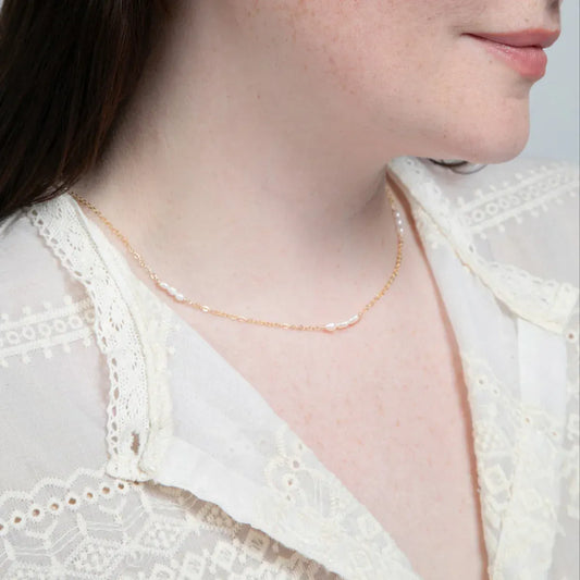 A woman in a white lace top showcasing a 14k gold filled necklace with freshwater rice pearl stations.