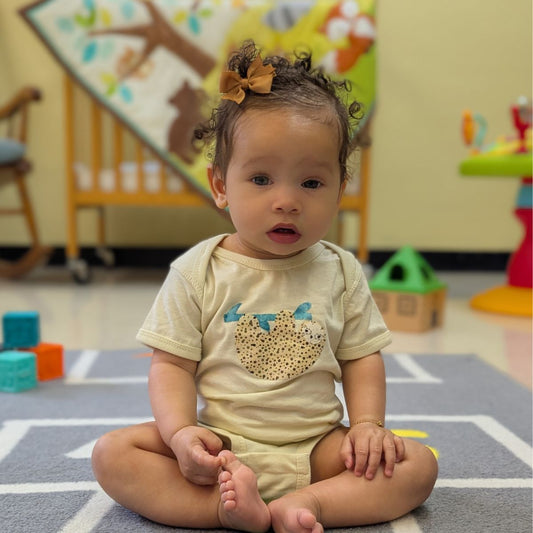 Beige baby onesie with a sloth design on a white background