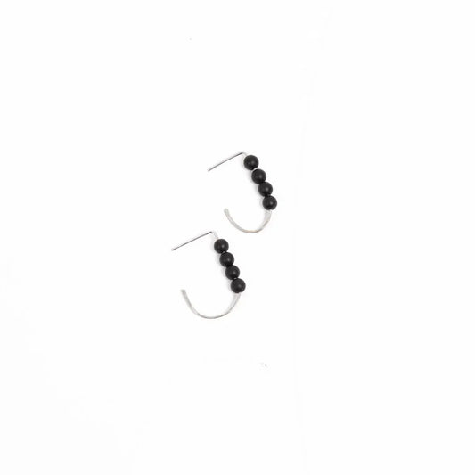 Woman in a yellow sweater wearing sterling silver j hoop minimalist earrings with four black onyx beads.