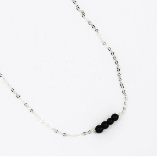 silver chain link necklace with four black onyx beads at the center on a whilte background