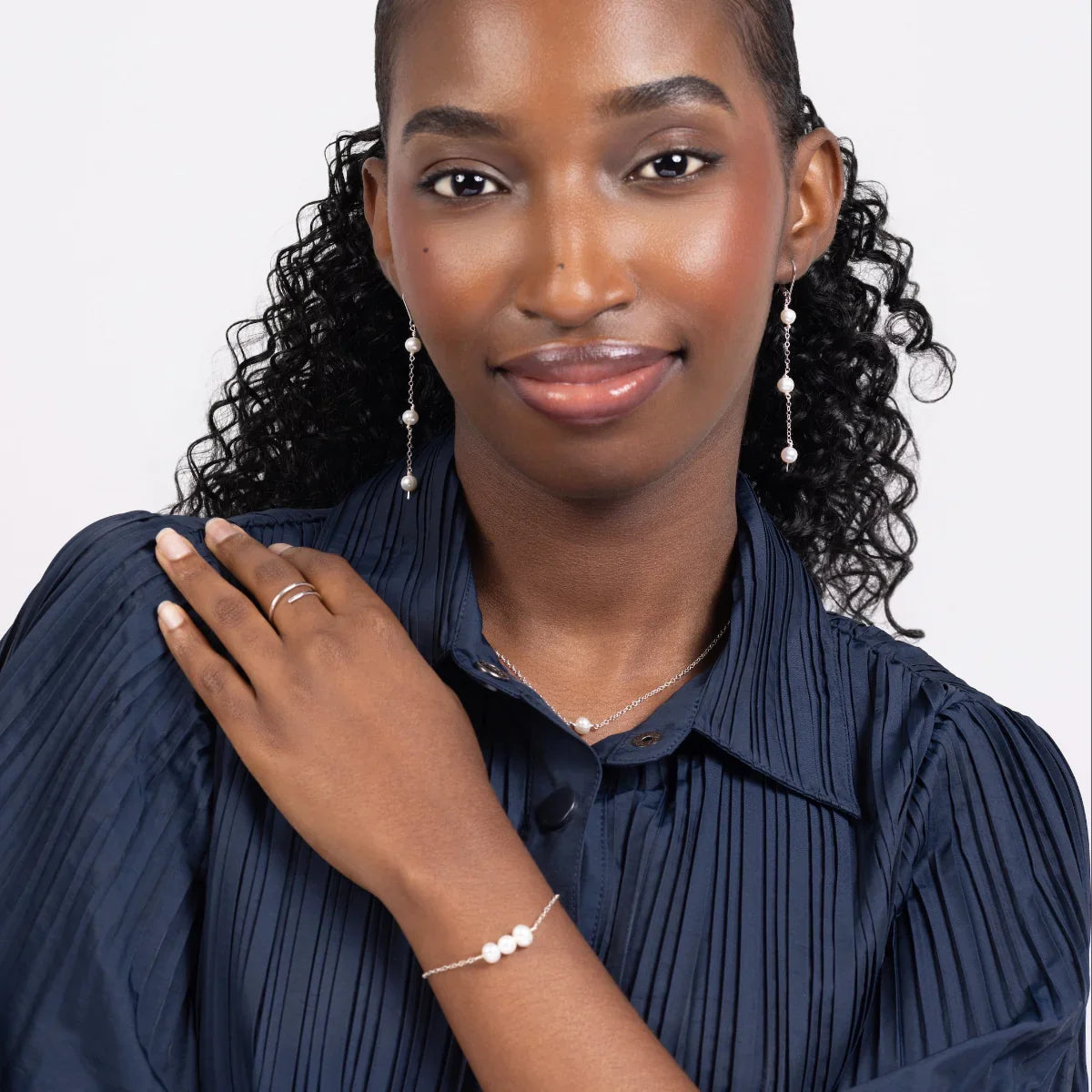 Woman in a blue pleated blouse wearing freshwater pearl triple drop leverback earrings, bracelet and necklace in sterling silver