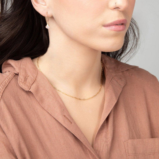 A woman wearing a light brown blouse showcasing a delicate minimalist paperclip chain necklace in 14k gold filled.