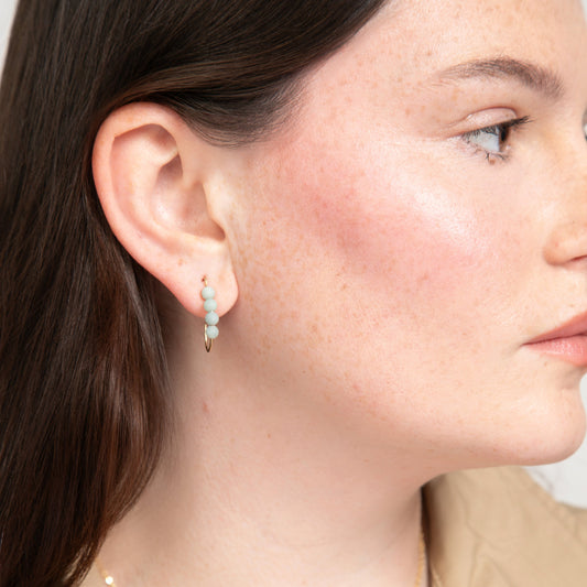 Close-up of a woman wearing a J hoop aarring with four small round amazonite gemstones.
