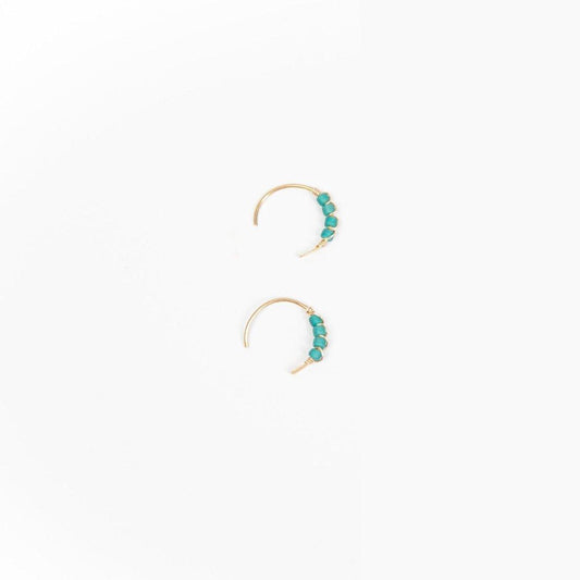 A close-up image of a woman's ear wearing a Moab Western Beaded Earring in 14k gold filled. The style is a hoop earring with turquoise beads. She is also wearing an ear cuff and huggie earring.