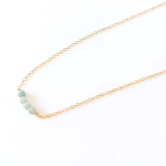 Close-up of woman in beige zippered top wearing a minimalist14k gold filled necklace with four amazonite gemstones.