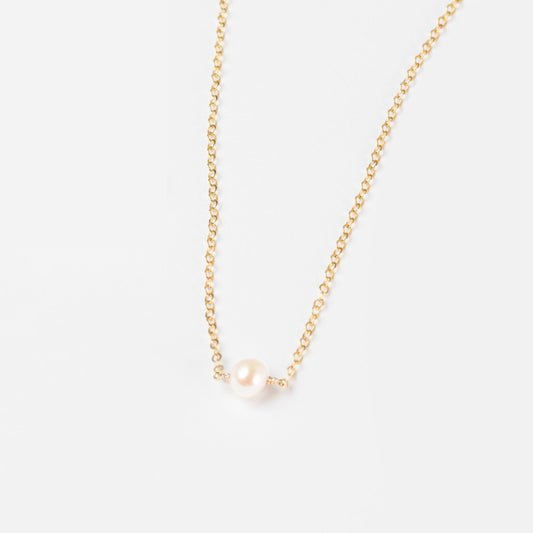 A woman in a white sweater wearing the Leeda Pearl Necklace, a dainty 14k gold filled necklace with a single freshwater pearl.
