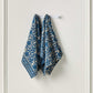 Two blue patterned towels hanging on a white rack against a light gray wall.